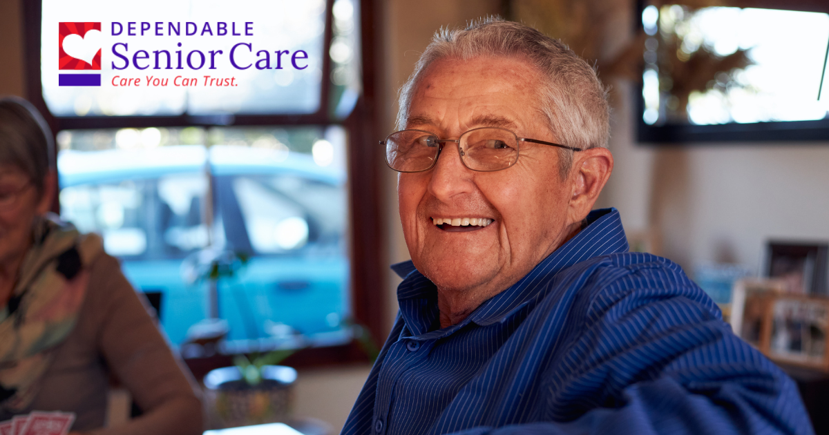 Smiling senior man sitting at a table and is happy as a result of successful long-distance caregiving.
